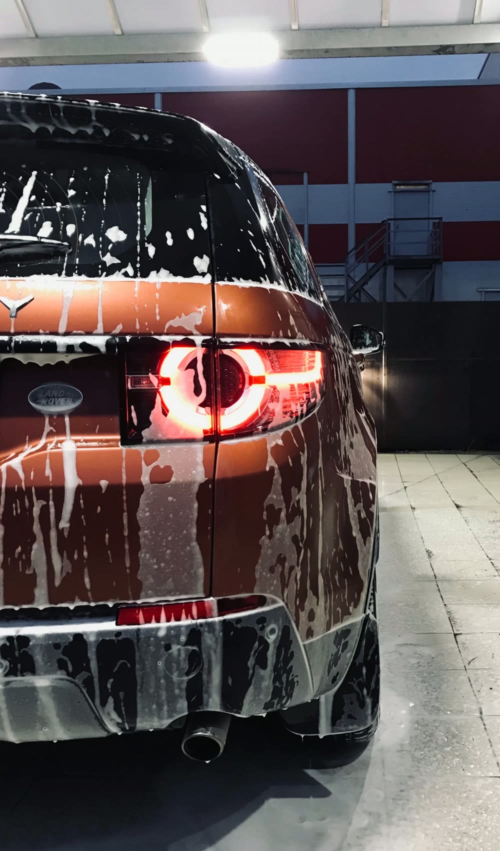 Suds running down the rear of a vehicle in a wash bay before coating