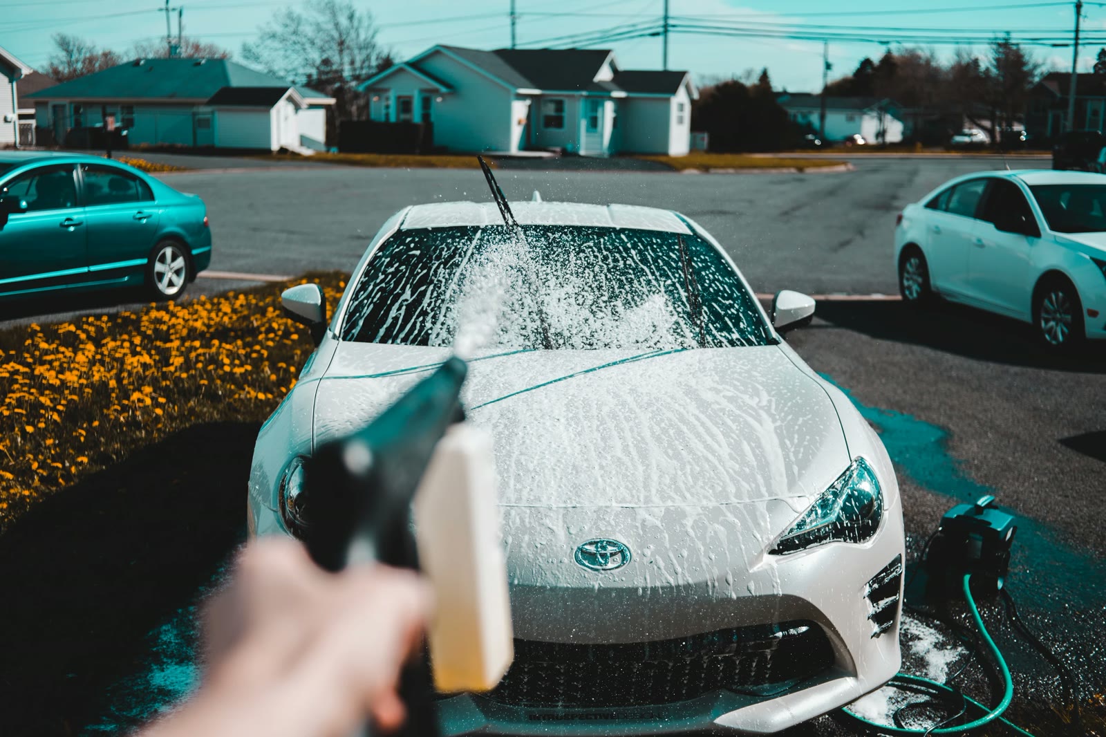 First-person view of a foam cannon rinsing a car on a sunny residential street