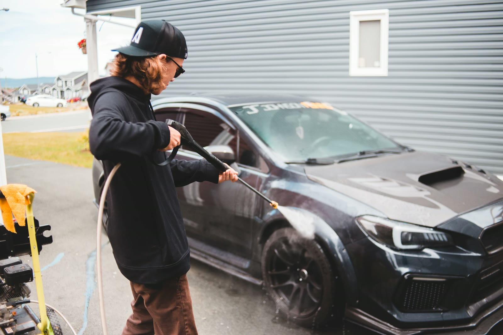 Detailer pressure washing a car wheel and fender in a driveway
