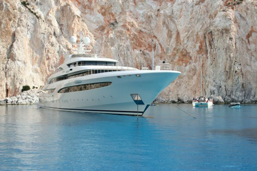 Large white yacht anchored in turquoise water below cliffs